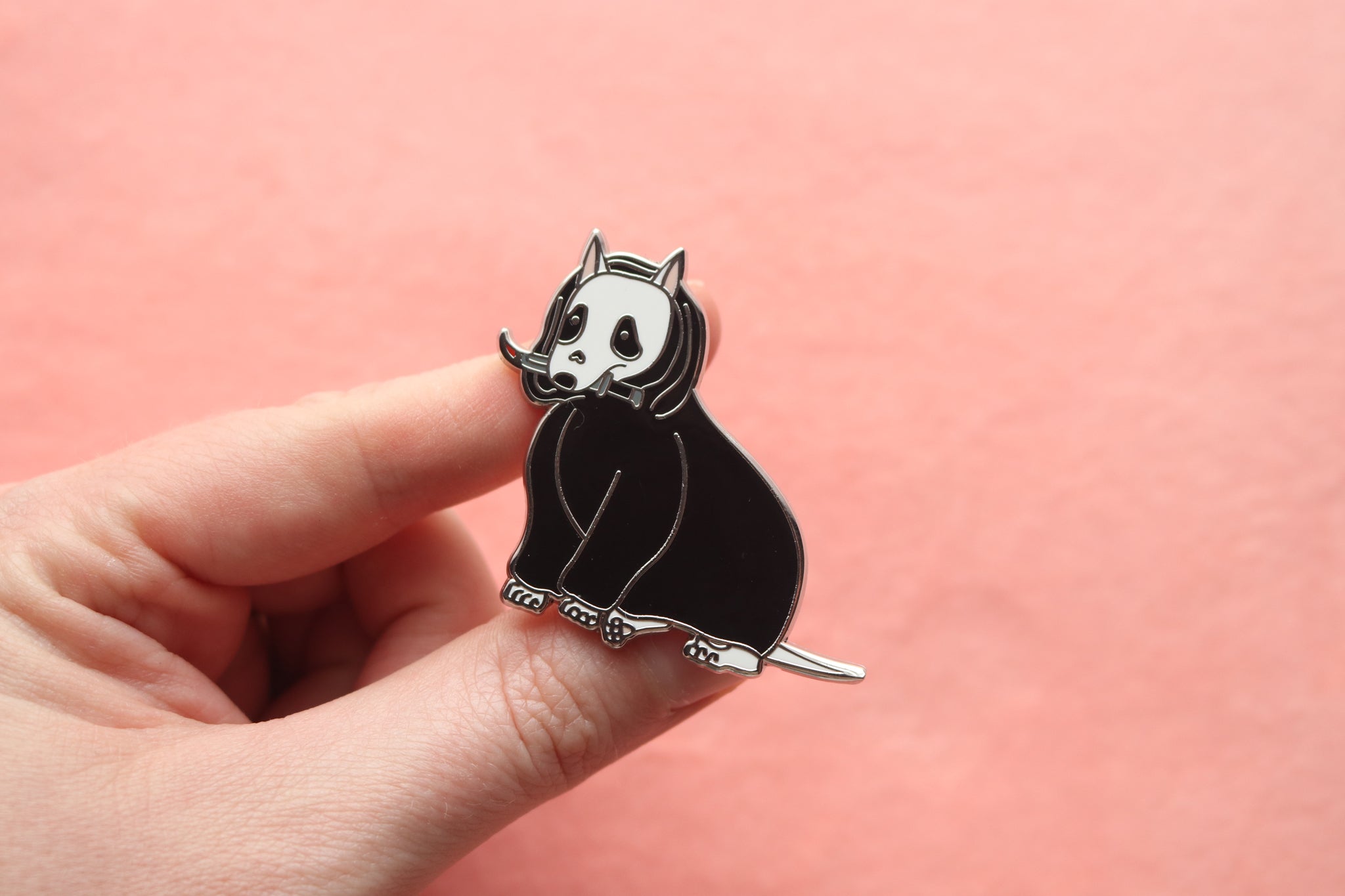 Hand holding an enamel pin of a Bull Terrier holding a bloody dagger and wearing a black cloak.