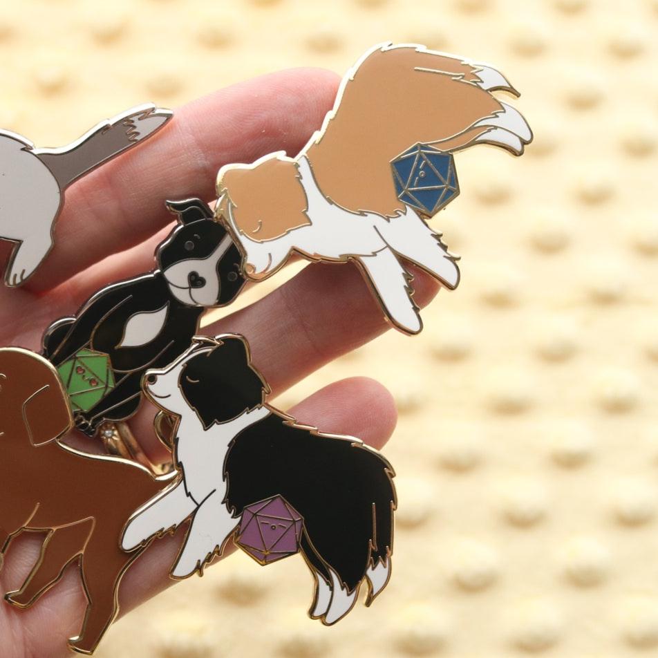 Hand holding a variety of dog pins including a light brown border collie and black and white border collie.