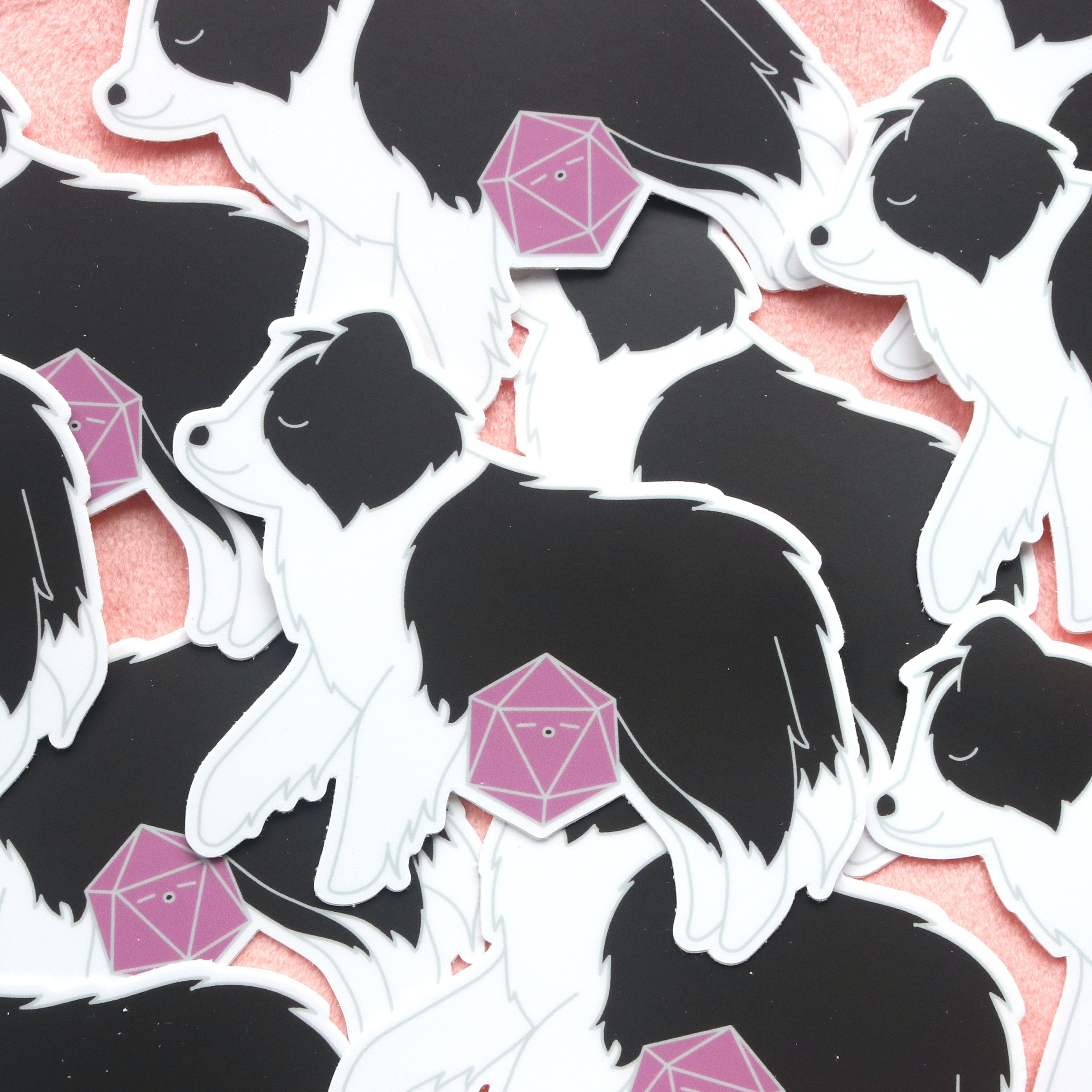 Pile of black and white border collie stickers. The dog is sleeping and a mauve d20 is cuddled up in it's lap.