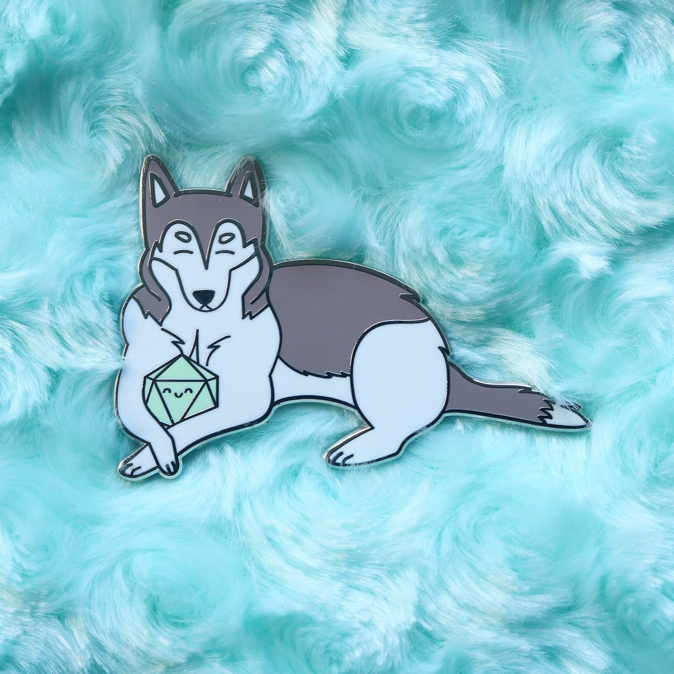 Gray and white husky enamel pin. Dog is holding a mint colored d20 between its front paws. Both dog and dice have happy faces with closed eyes.