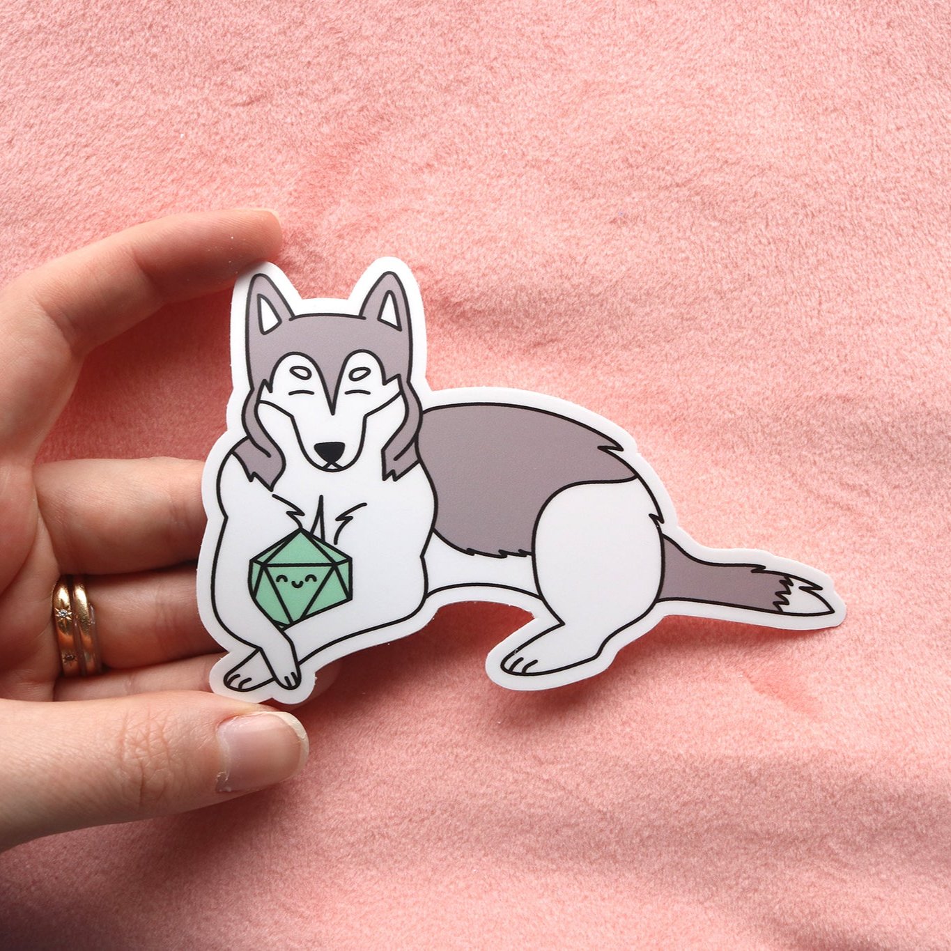 Gray and white husky sticker. Dog is holding a mint colored d20 between its front paws. Both dog and dice have happy faces with closed eyes.