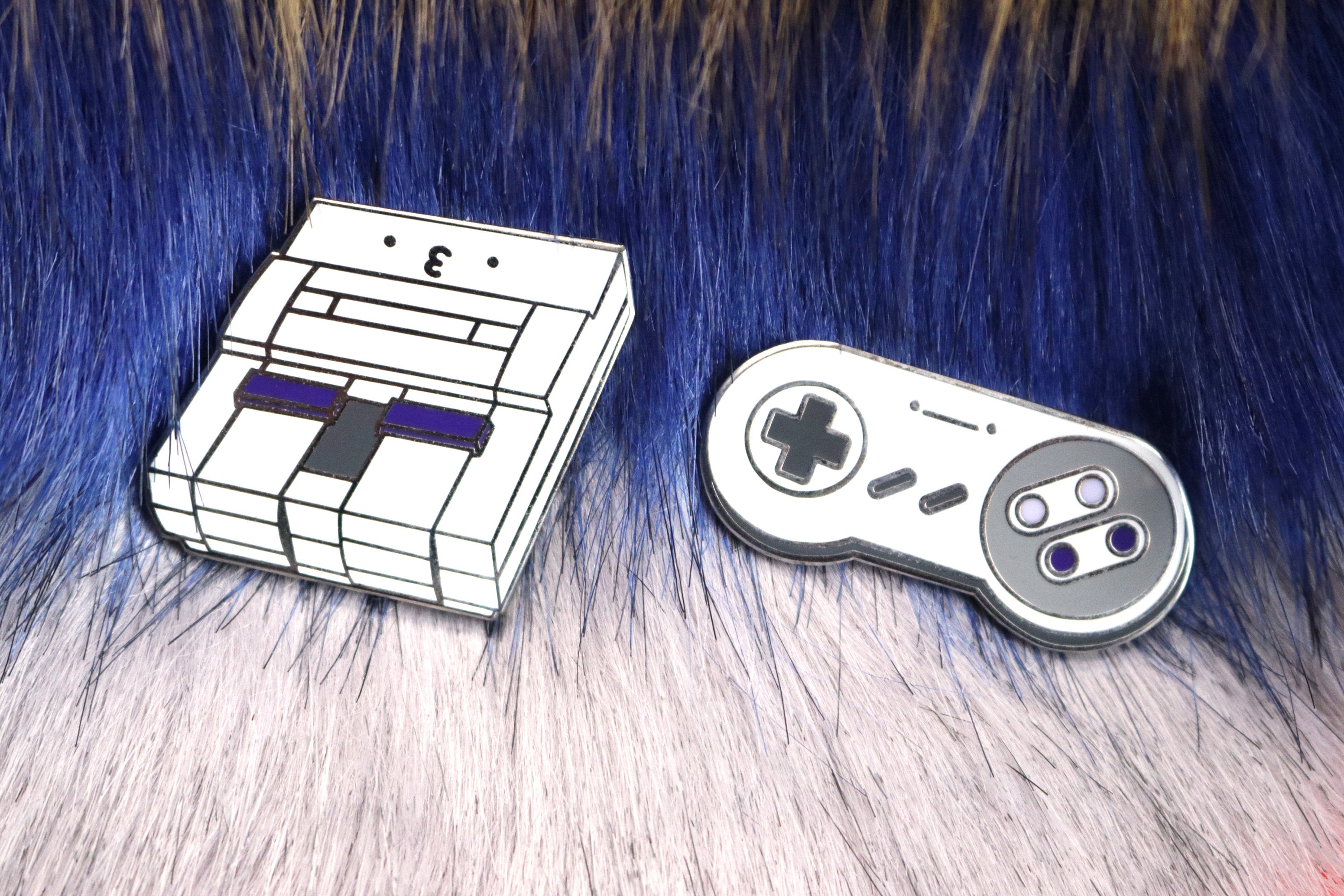 SNES Console and Controller Hard Enamel Pins on Blue and Pink Fur Background