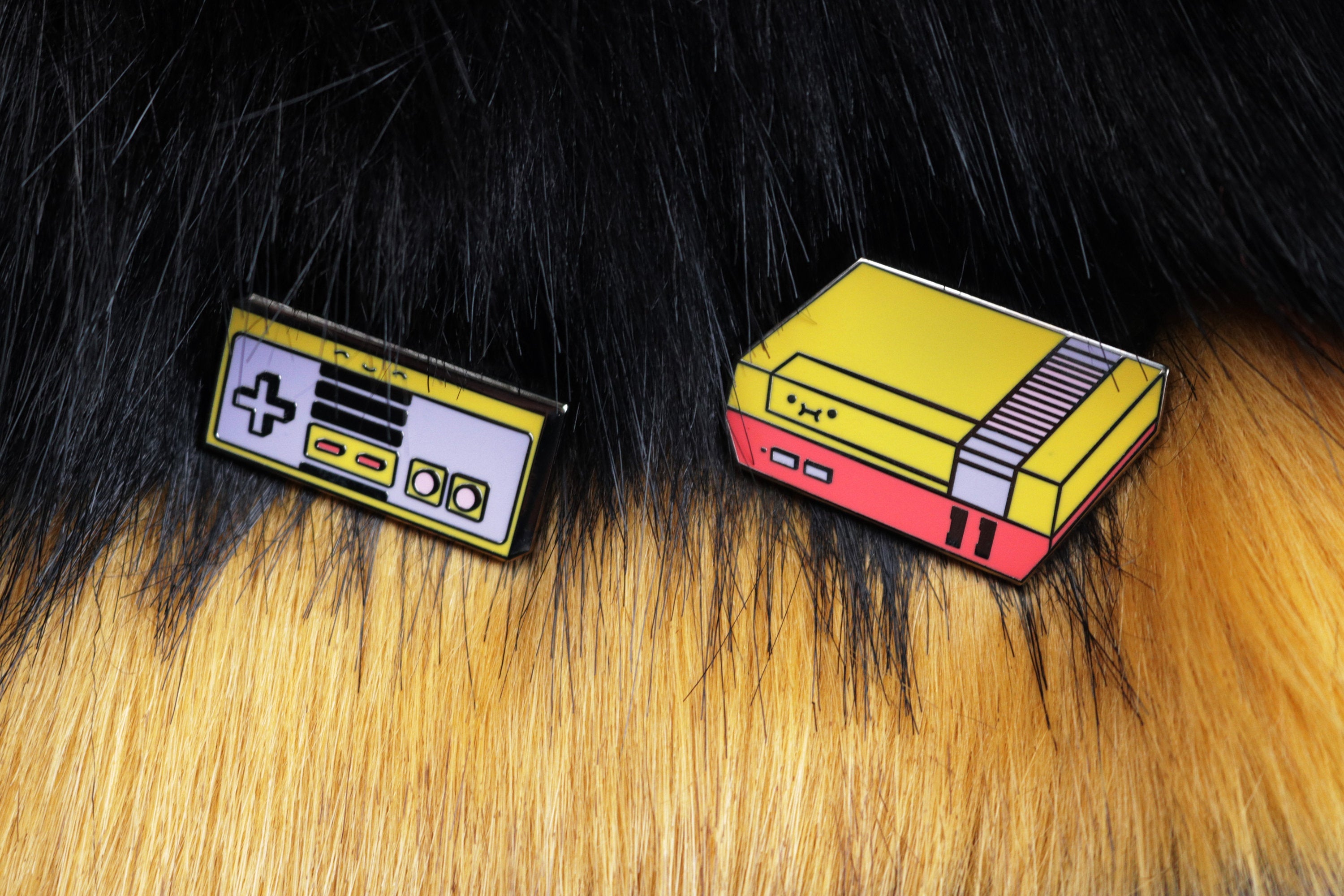 Yellow, Purple, Red, and Pink Custom NES Console and Controller Hard Enamel Pins on Black and Yellow Fur Background