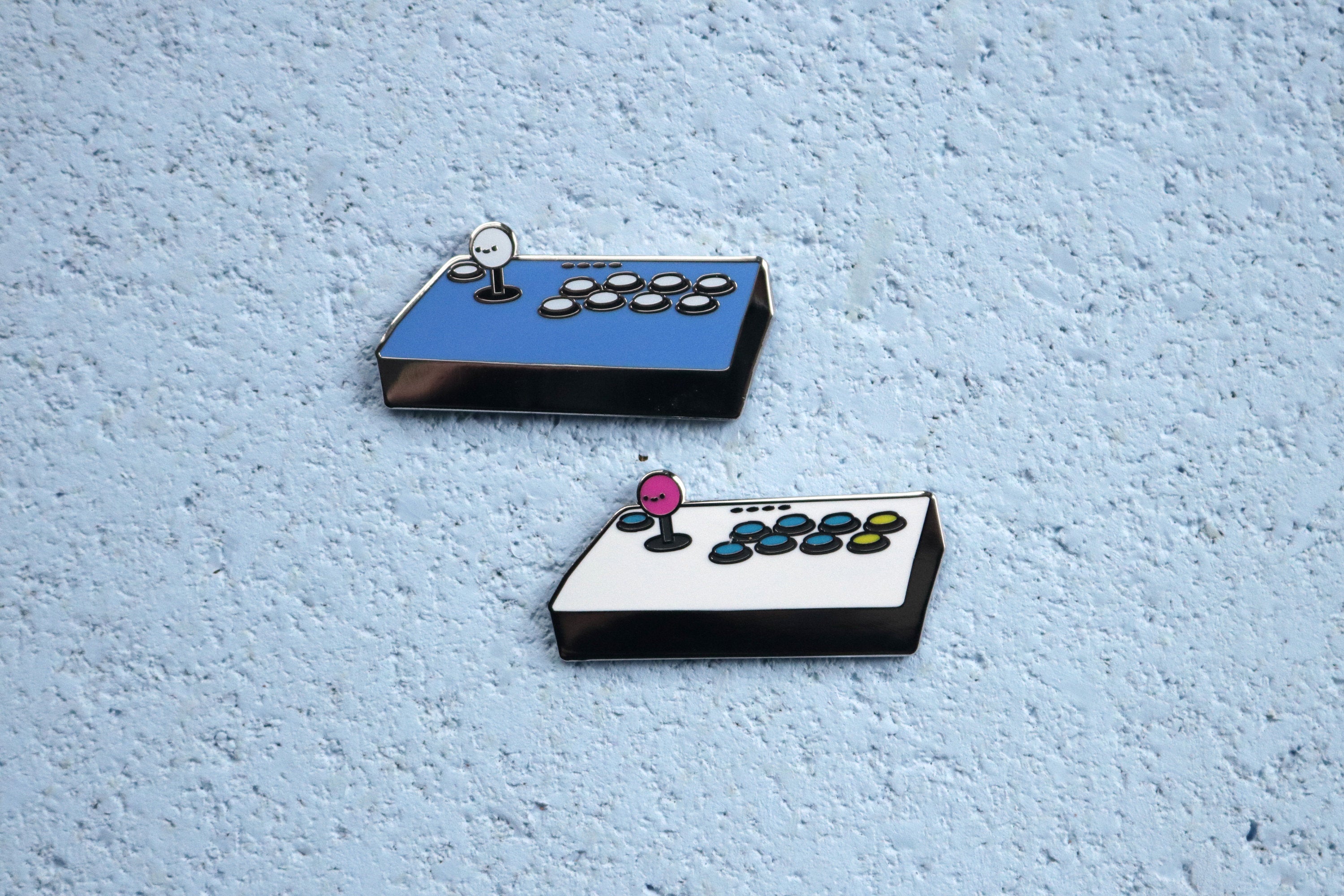 Blue and White Fight Stick Hard Enamel Pins on Blue Cork Board